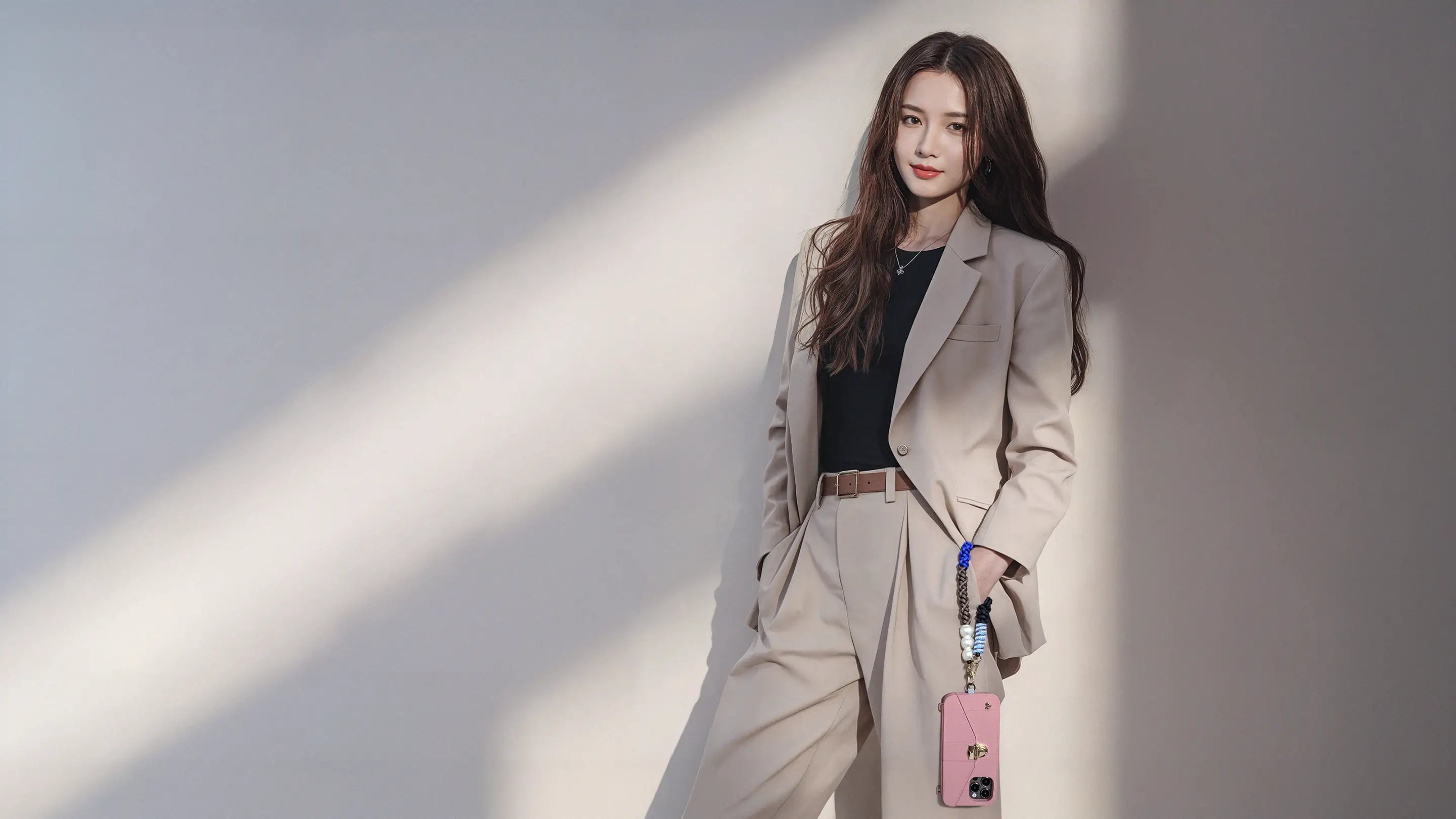 Confident office lady leaning against wall with Hades HAND-BRAIDED TENCEEL™ WRISTLET dangling AURA PURSE CASE in Burlwood. DISCOVER STRAPS THAT INSPIRE.