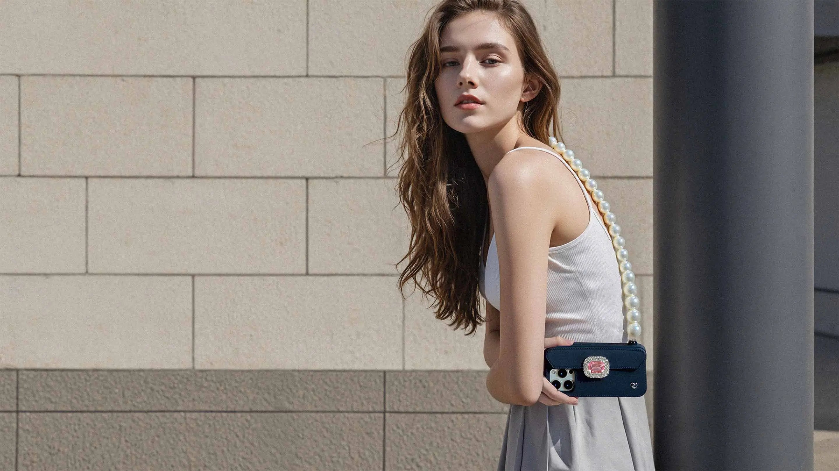 Fashion-forward woman wearing minimalist white tank top with pearl crossbody strap connected to black STYLEBASE PURSE CASE featuring Eterna-Royal ornament. CRAFT YOUR UNIQUE STYLE.